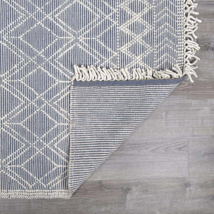 Close up of the Ramsbury Denim Blue Wool Rug showing geometric pattern, fringe detail, and backing. Fold