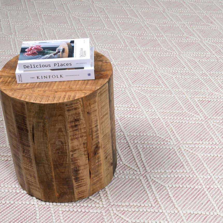 Close-up of Ramsbury Soft Pink Wool Rug's geometric design and texture next to a wood side table with books. Styleshot