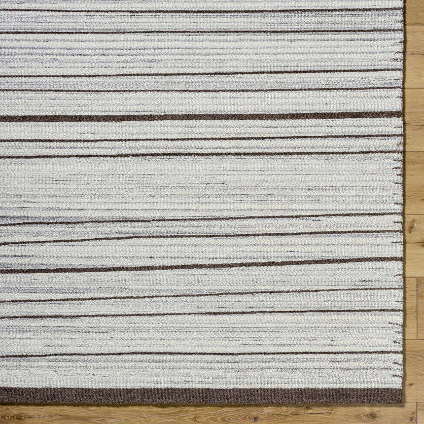 Close-up of the hand-tufted Cliona Area Rug. Wool rug with charcoal, ivory, and taupe horizontal stripes. Corner