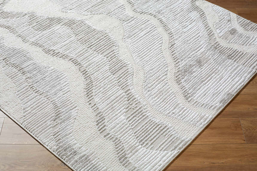 Close-up of Aniela area rug. Contemporary style with cream, ivory, and gray textured wave pattern on wood floor. Corner
