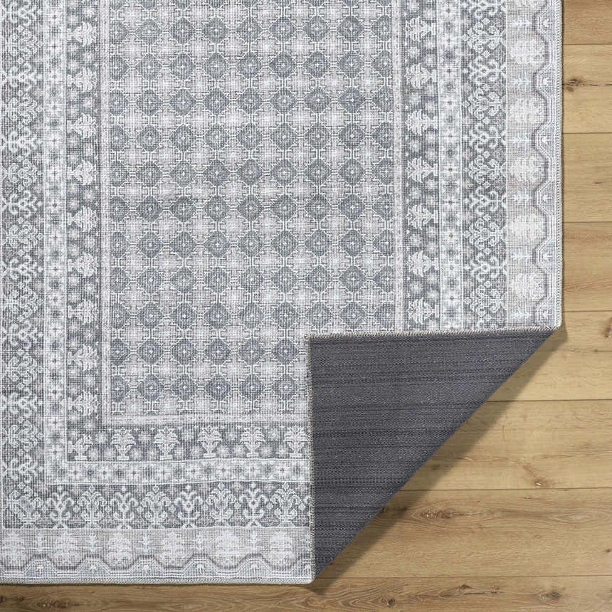 Close-up of Rainier Gray Washable Rug showing its traditional pattern, off white, pale blue, sage, and tan colors. Machine woven texture. Fold