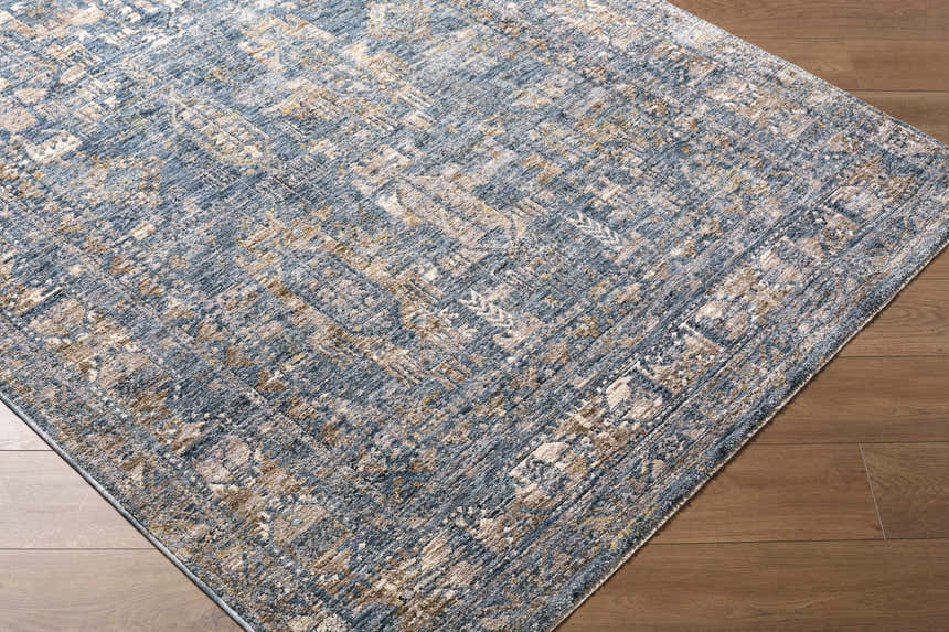 Close-up of the Mirabel Denim Blue Traditional Rug showing its blue, cream, and brown distressed pattern on a wood floor. Corner