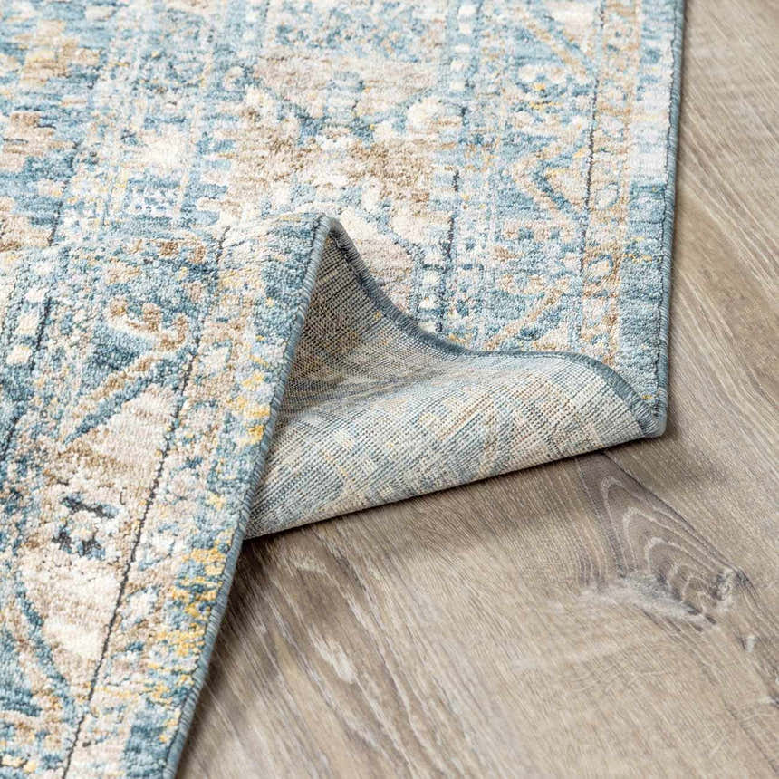 Close-up of the Mirabel Denim Blue Traditional Rug showing its blue, cream, and brown pattern and the rug's backing. Fold