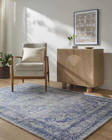 Entryway scene with a blue and ivory Csilla Area Rug, gray chair, and light wood cabinet. Roomscene-Rectangle