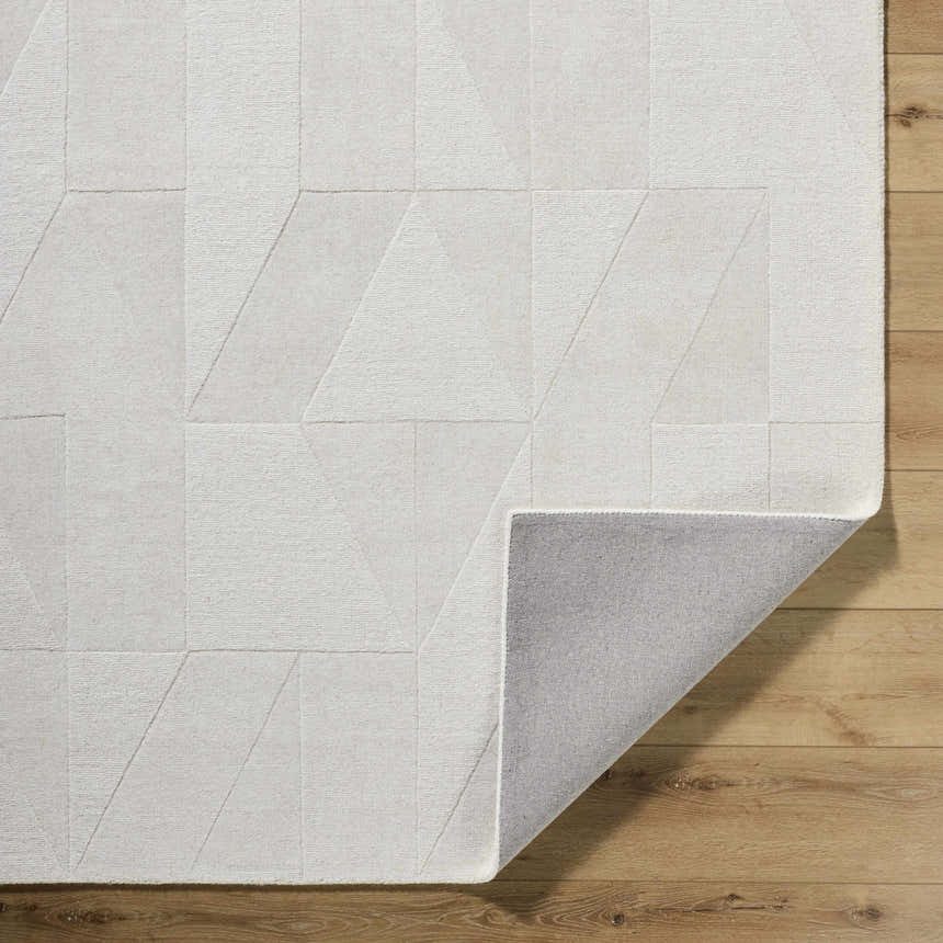 Close-up of the ivory Callie Area Rug showing geometric pattern, wool texture, and gray backing on wood floor. Fold
