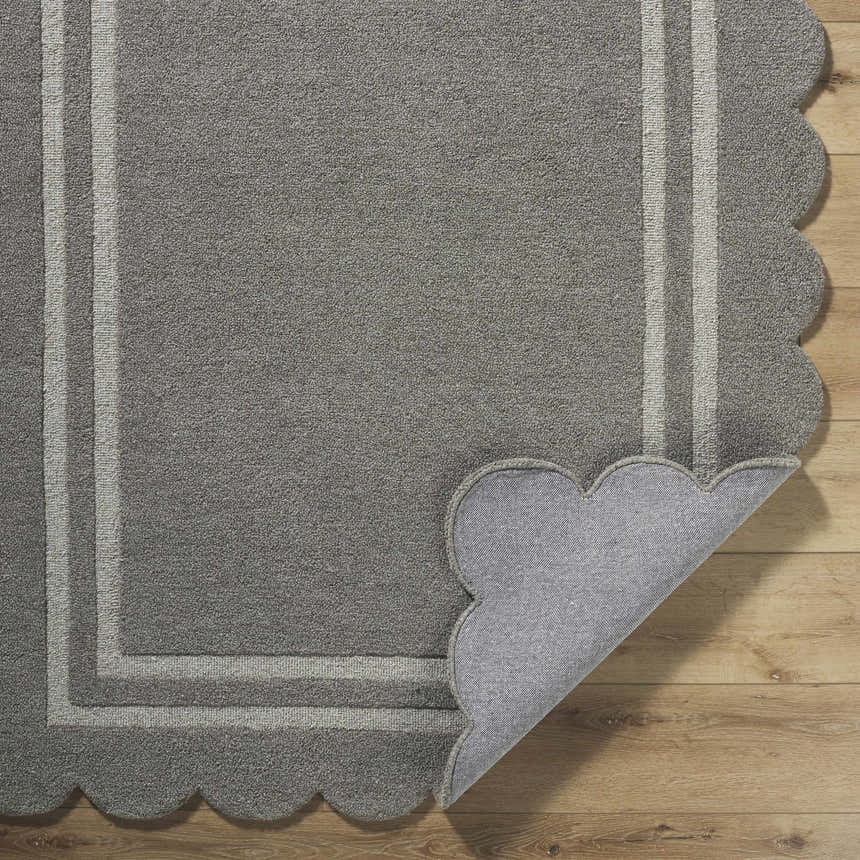 Close-up of the hand-tufted Chogan Stone Gray Area Rug showing wool texture, striped border, and scalloped edge. Fold
