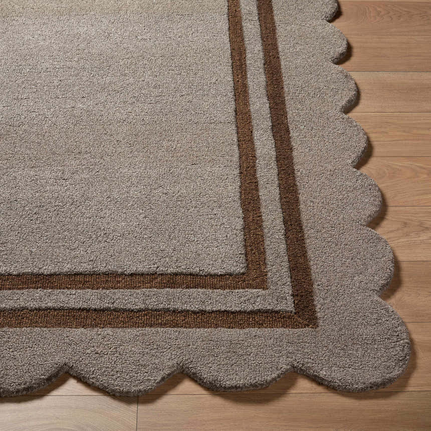 Close-up of the hand-tufted Chogan Charcoal Area Rug featuring a brown border and a scalloped edge on hardwood floors. Front