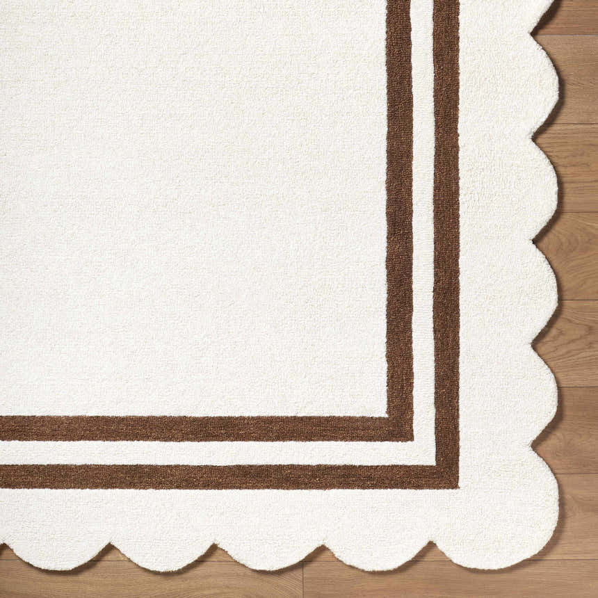 Close-up of the hand-tufted Chogan Ivory Area Rug, featuring a brown border and a scalloped edge detail. Corner