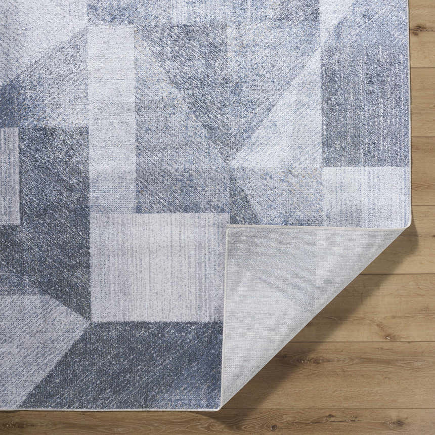 Close-up of the Chachi Washable Geometric Rug showing the gray, light gray, and navy geometric pattern and woven texture. Fold