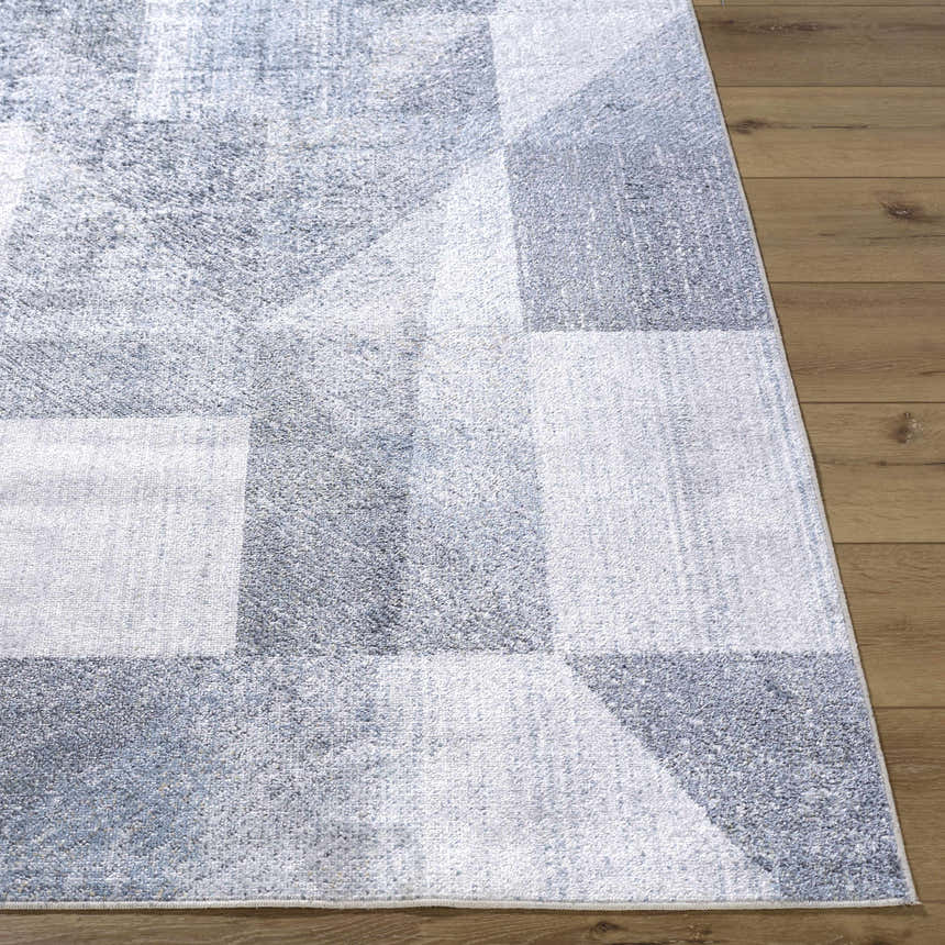 Close-up of the Chachi Washable Geometric Rug. Features gray, light gray, and blue tones in a modern geometric pattern. Front