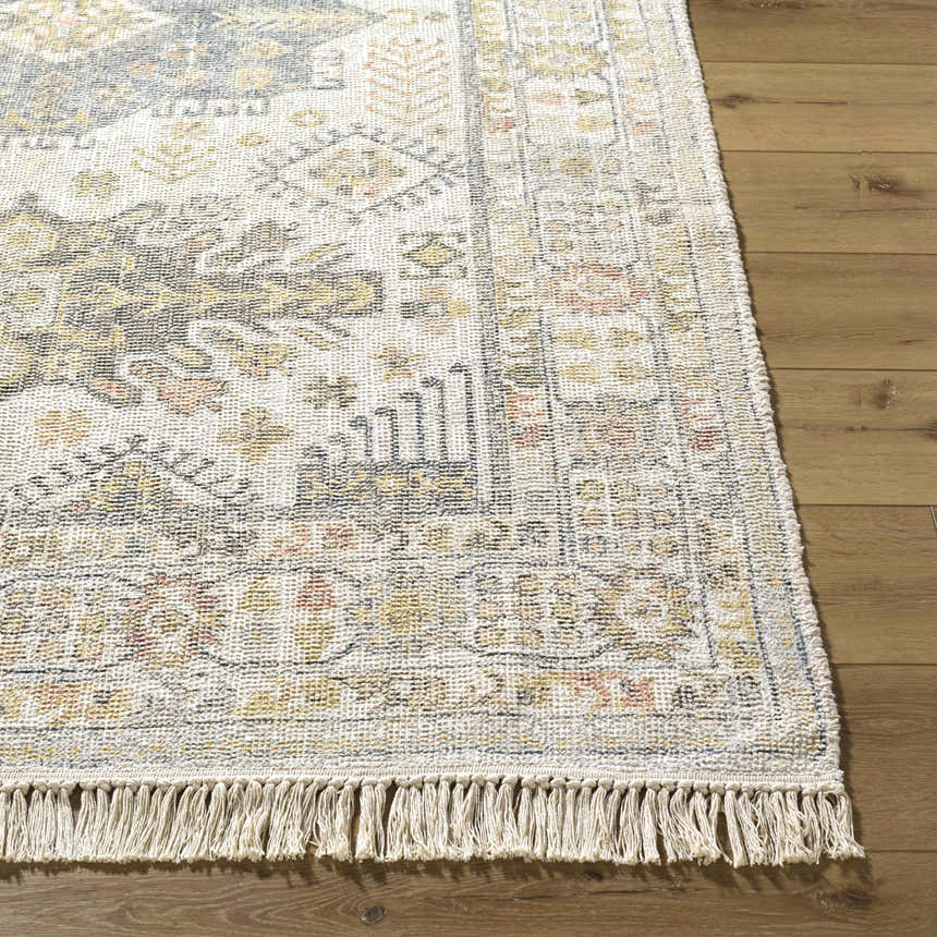 Close-up of the hand-loomed Chaela Ivory & Olive Area Rug on wood floor. Features blush, mustard, and slate blue colors. Front
