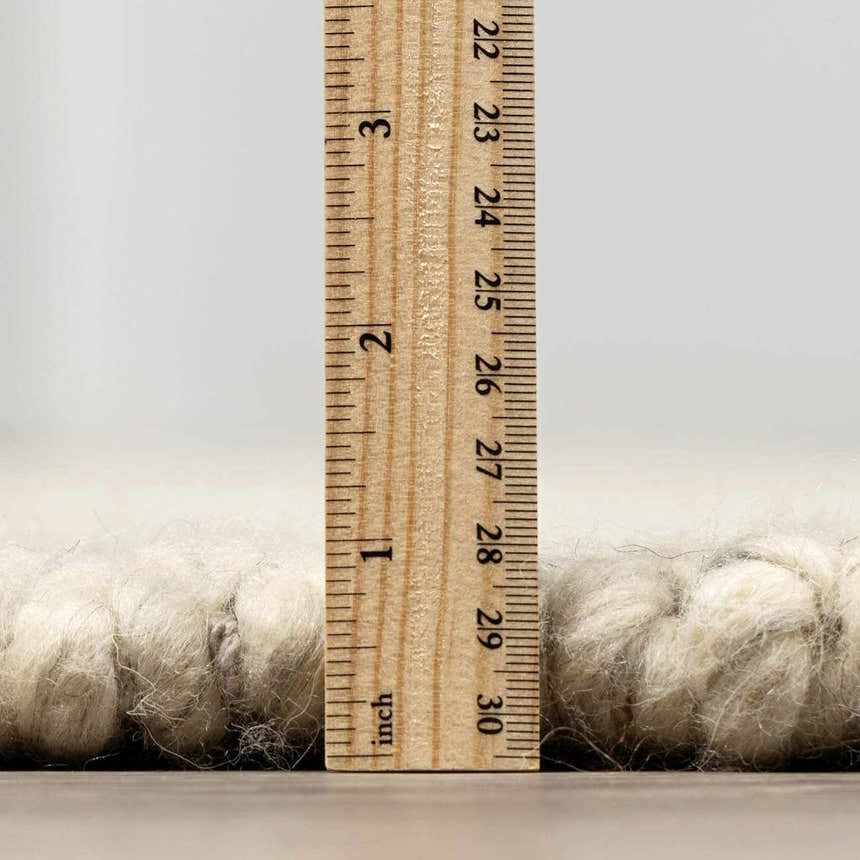 Close-up of the Clarke Textured Braided Stripe Rug in dark beige, showing the rug's thickness with a ruler. Pile