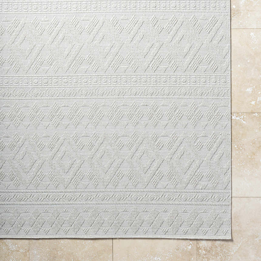Close-up of the light silver Choire Area Rug, showcasing its geometric pattern and woven texture. Corner