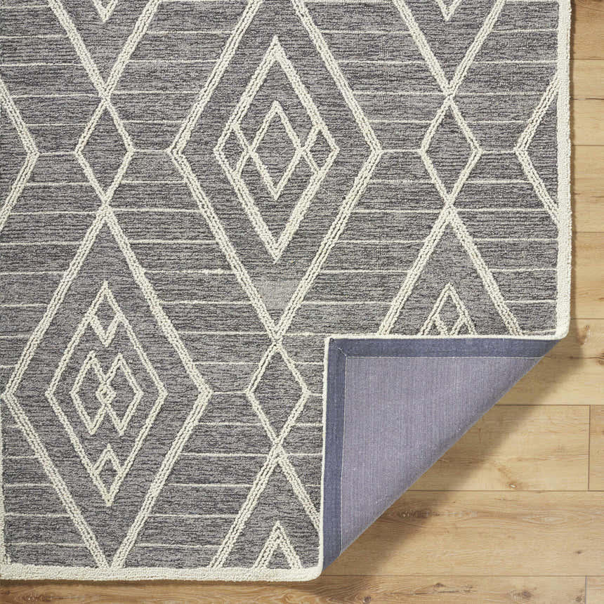 Close-up of the Ceanna Area Rug. Gray wool rug with off-white geometric diamond pattern. Hand-tufted texture. Fold