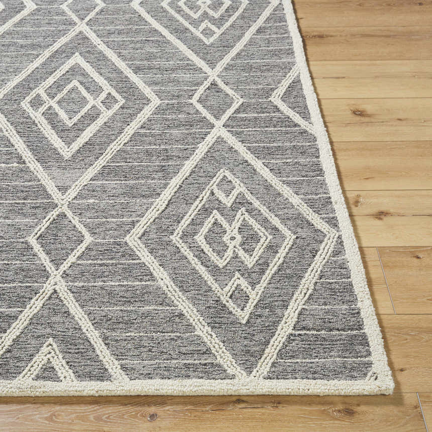 Close-up of the Ceanna Area Rug. Gray wool rug with off-white geometric diamond pattern on light wood floor. Front