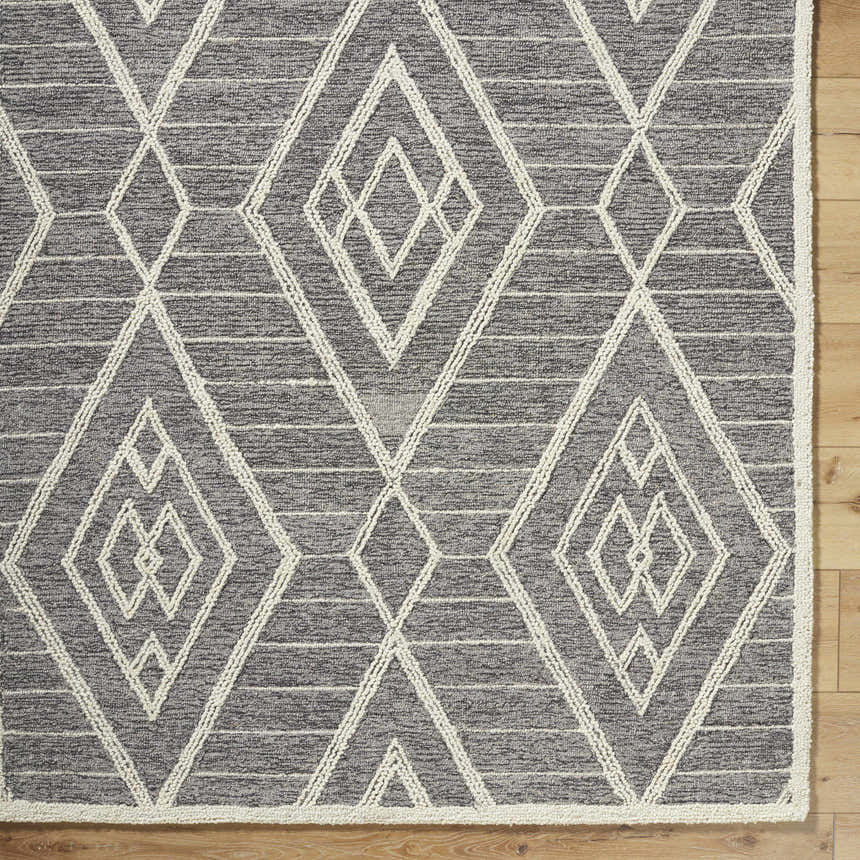 Close-up of the Ceanna Area Rug; gray wool with off-white geometric diamond pattern and textured hand-tufted construction. Corner