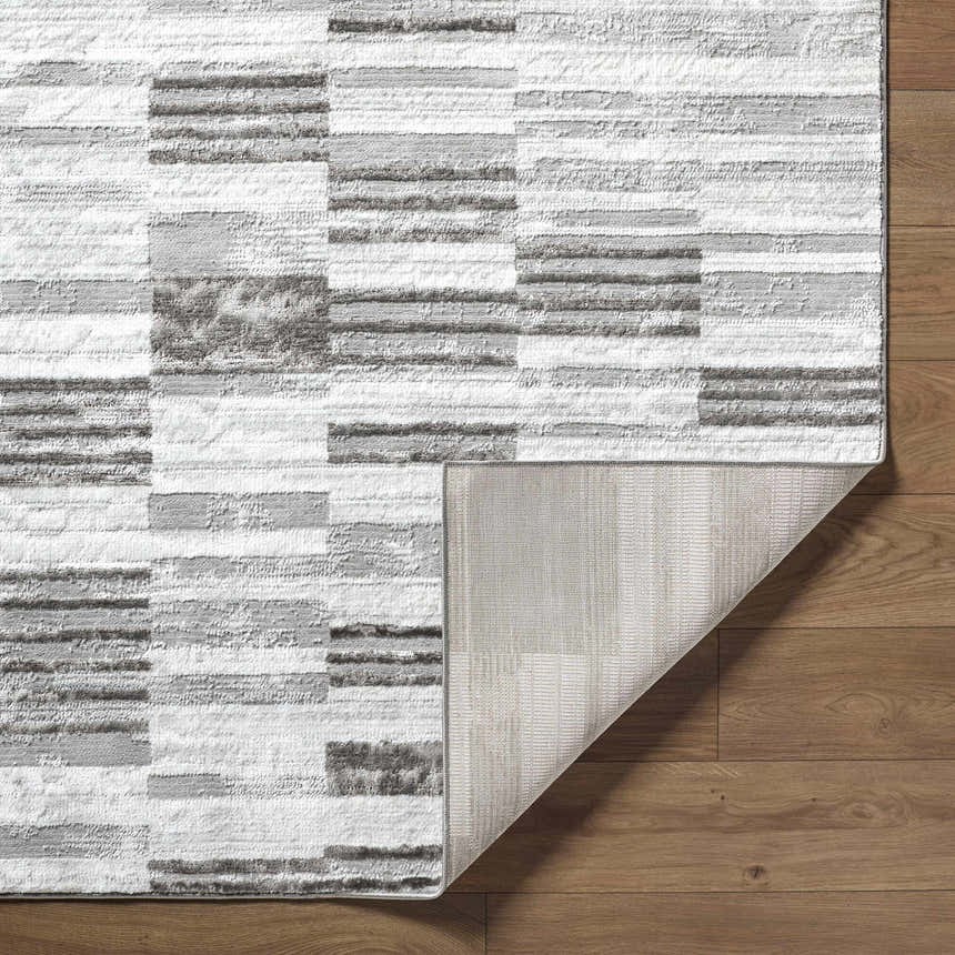 Close-up of the Chiaki Light Gray Area Rug showing its geometric pattern, texture, and backing on wood floor. Fold