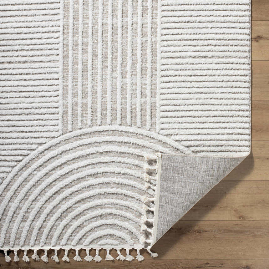 Close-up of the Cassie Area Rug showing cream and peach stripes and semicircle design with tassels on a wood floor. Fold