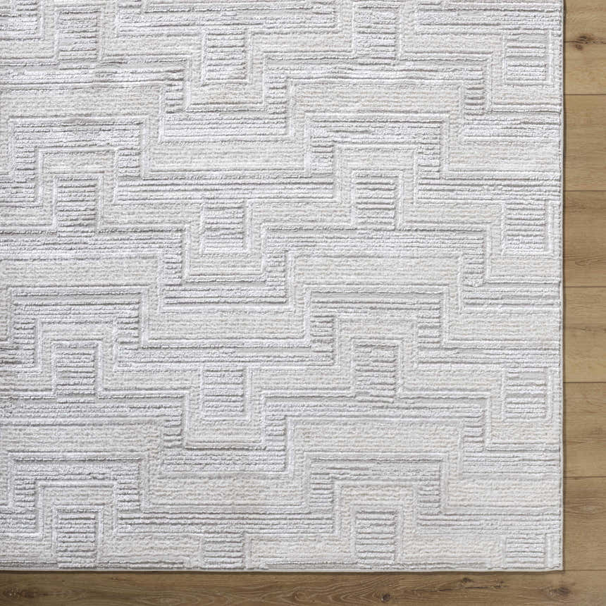 Close-up of the Cormac Area Rug, a cream and ivory rug with a contemporary geometric pattern on wood flooring. Corner