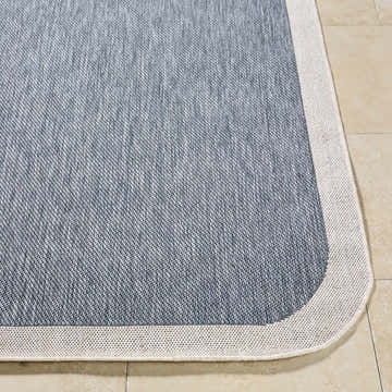 Close-up of the Chetan Blue Outdoor Rug showing its woven texture and cream border on a tile floor. Front