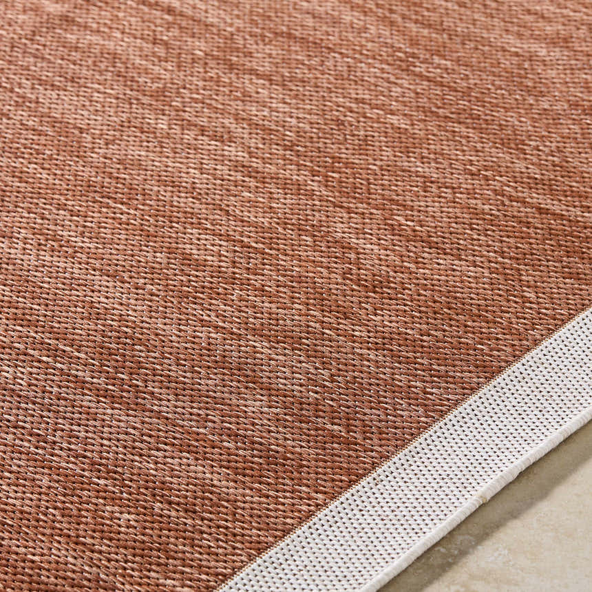 Close-up of the Chetan Brown Outdoor Rug showing its woven texture and brown, burnt orange, and cream colors. Texture