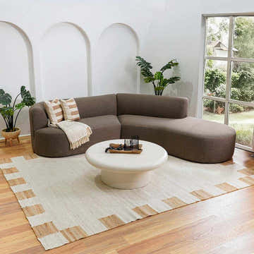 Living room scene with a Rocio White Jute Carpet, brown sectional sofa, and round coffee table. Neutral, modern aesthetic. Roomscene-Rectangle
