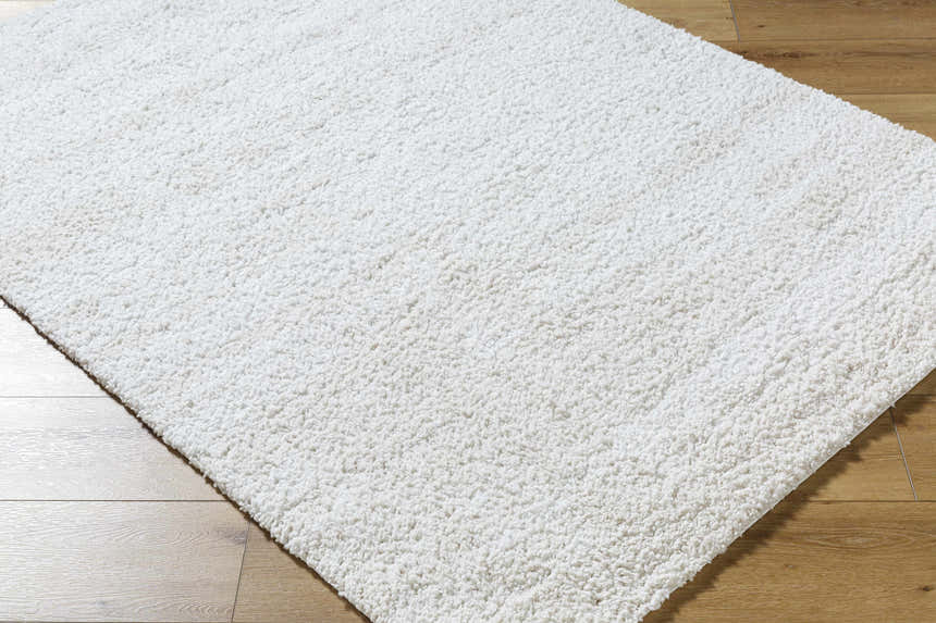 Close-up of the Arlind Area Rug, a white shag rug with a soft, textured pile on wood flooring. Corner