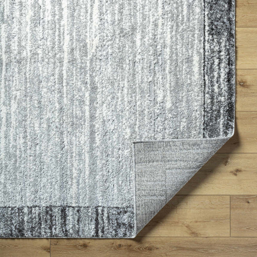 Close-up of Dhaval Black Area Rug showing charcoal, light gray colors, and machine woven texture on wood floor. Fold
