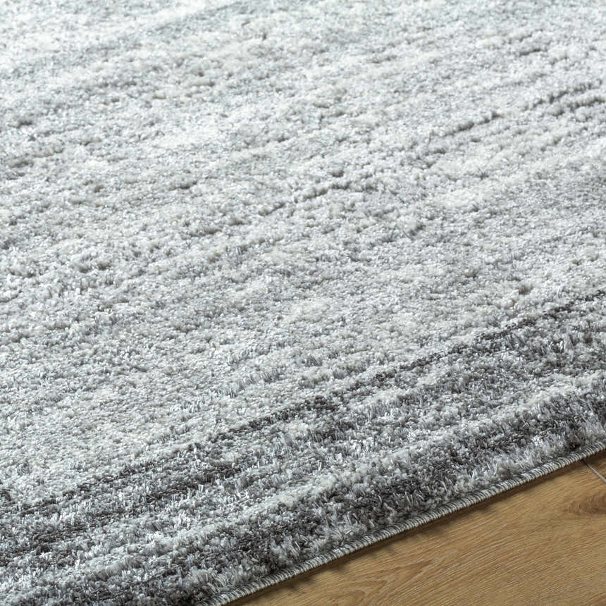 Close-up of the textured Dhaval Black Area Rug with black, charcoal, and light gray hues on a wood floor. Texture