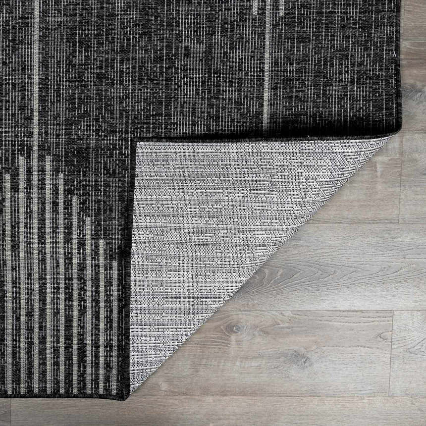 Close-up of the Stephan Area Rug showing its black, charcoal, and cream contemporary pattern and durable polypropylene material. Fold