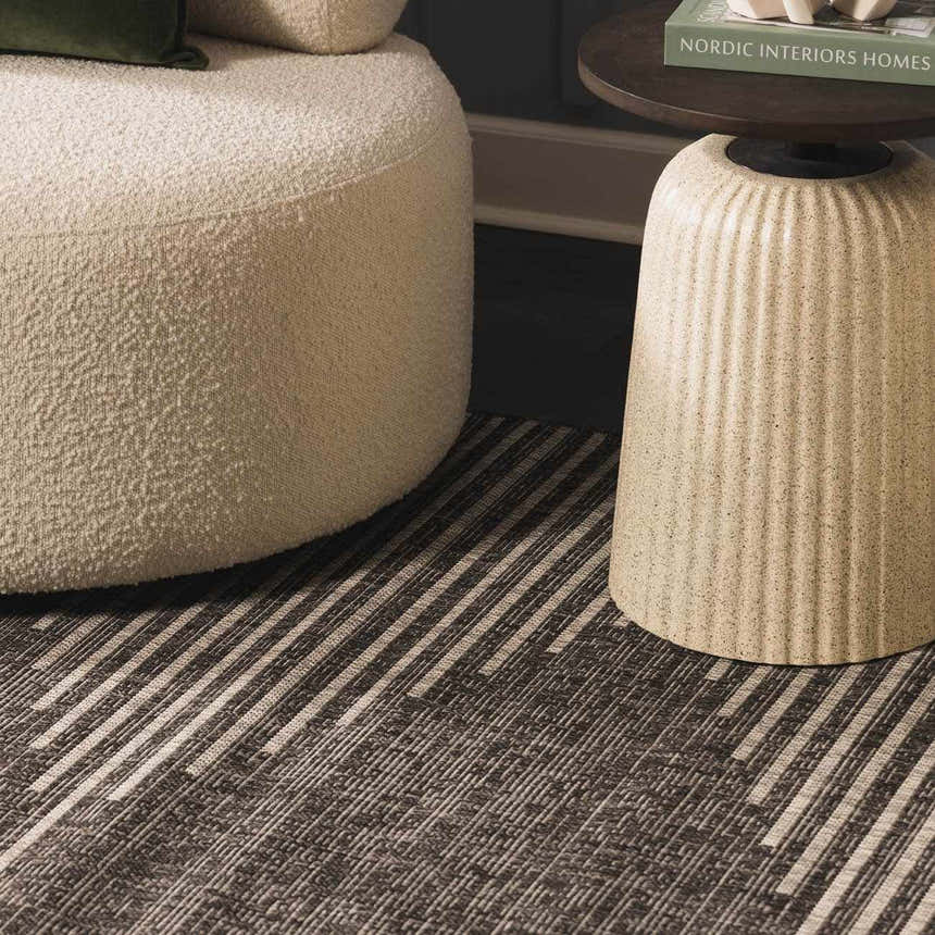 Close-up of the Stephan Area Rug in black, charcoal, and cream, styled with a cream boucle ottoman and side table. Styleshot