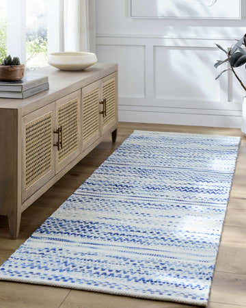 Entryway scene with a blue and white Flann Area Rug runner, light wood floors, and a cane cabinet. Roomscene-Runner