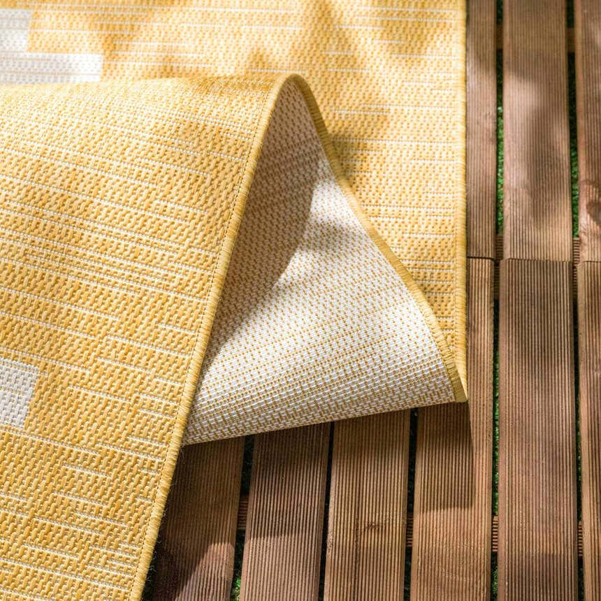 Close-up of the Djugun Yellow Outdoor Rug showing geometric weave, colors, and durable polypropylene material. Fold