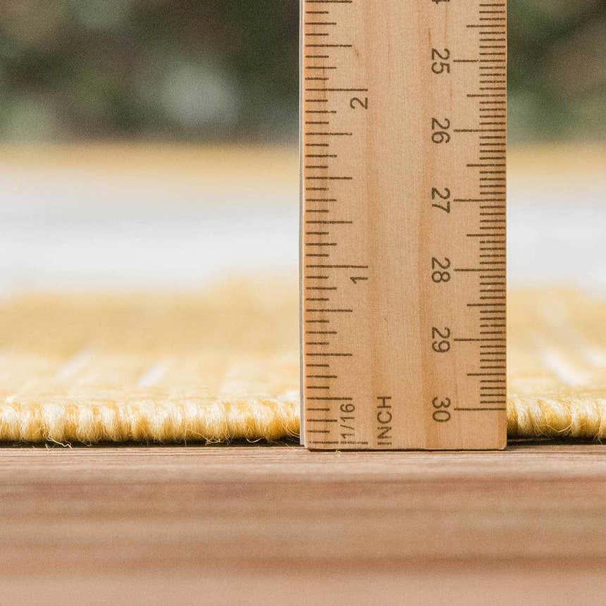 Close-up of the Djugun Yellow Outdoor Rug showing pile height with a ruler, revealing its texture and construction. Pile