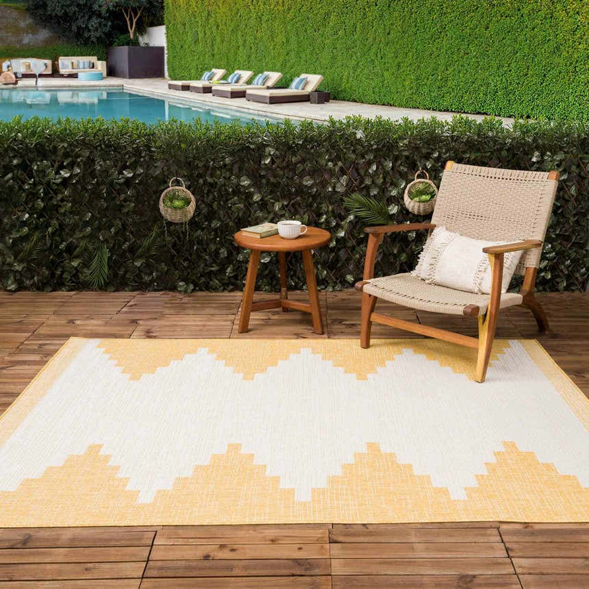 Outdoor patio scene with a Djugun Yellow rug, wooden chair, and table by a pool. Roomscene-Rectangle