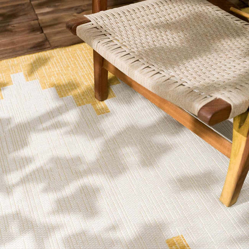 Close-up of the Djugun Yellow Outdoor Rug with geometric beige and yellow pattern, paired with a woven chair. Styleshot