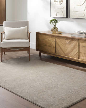 Living room scene with a Brockton Solid Gray Wool Rug, wood cabinet, armchair, and neutral decor. Roomscene-Rectangle