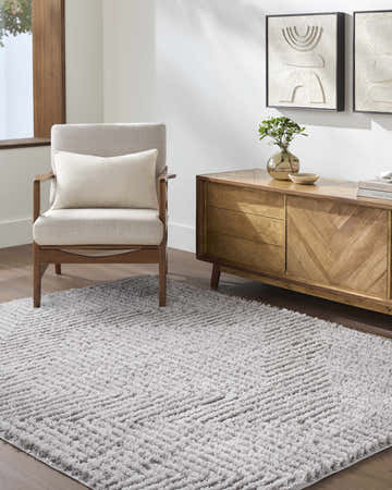 Living room scene with a light slate Ashlyn Area Rug, beige chair, and wood cabinet with abstract art. Roomscene-Rectangle