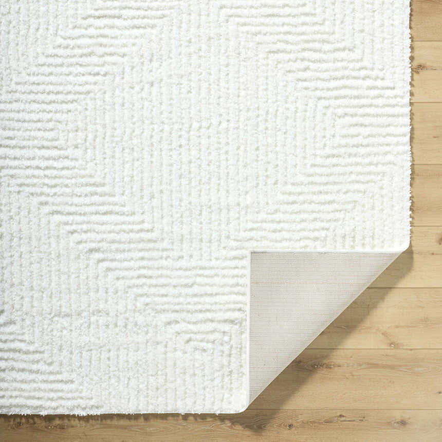 Close-up of the plush, cream Ashlyn White Area Rug featuring a subtle geometric shag design on light wood floors. Fold