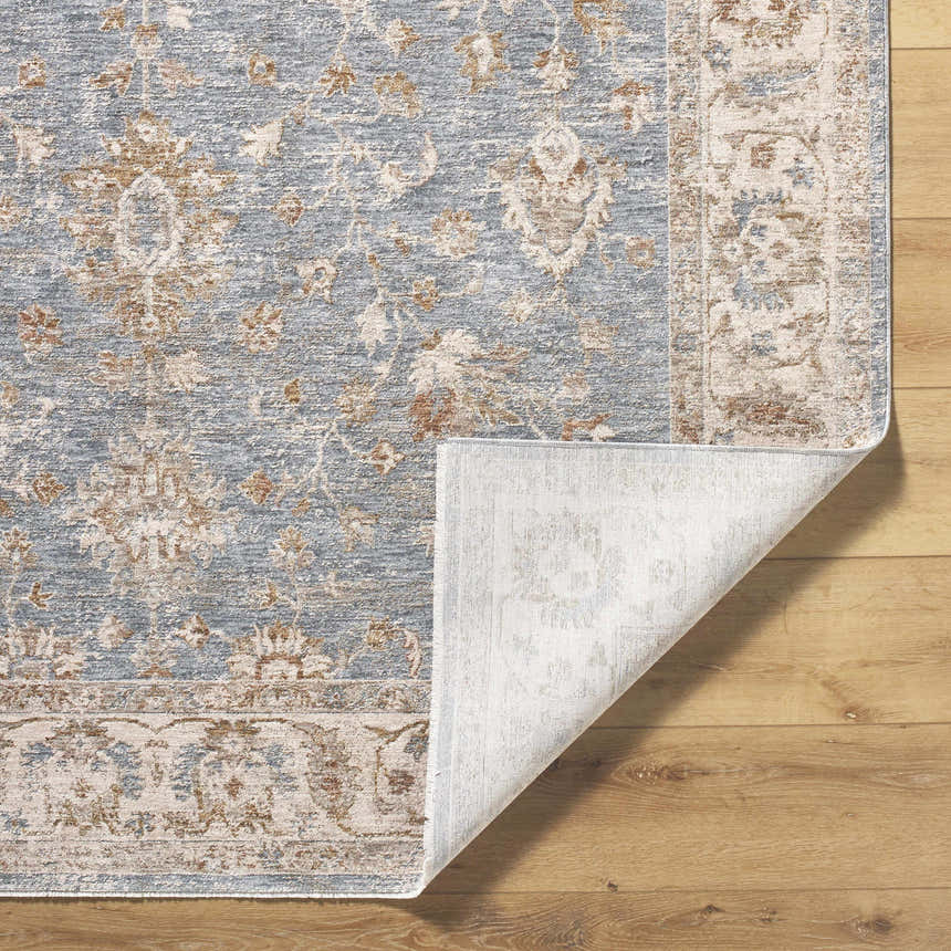 Close-up of the Avivit Sage Area Rug showing its blue, cream, and tan farmhouse floral pattern and folded corner. Fold
