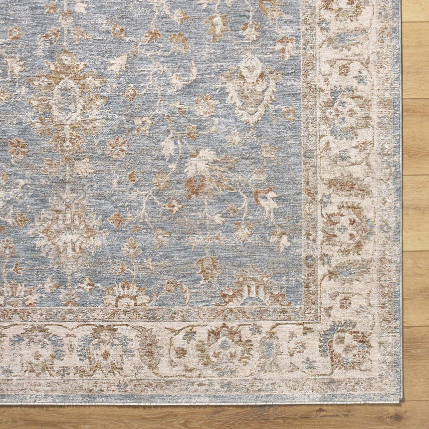 Close-up of the Avivit Sage Area Rug. Traditional floral design in blue, cream, tan, and gray on a wood floor. Corner