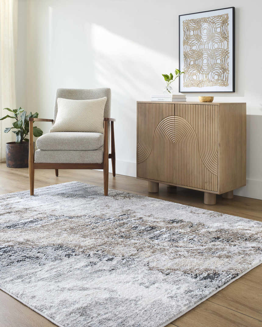 Living room scene with an Ashlee Area Rug in ivory, gray, and brown tones, styled with a gray chair and wooden cabinet. Roomscene-Rectangle