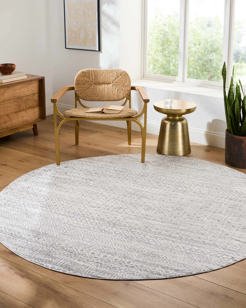 Sunlit living room with round Gravelbourg Washable Boho Rug, woven chair, wood floors, and brass side table. Roomscene-Round
