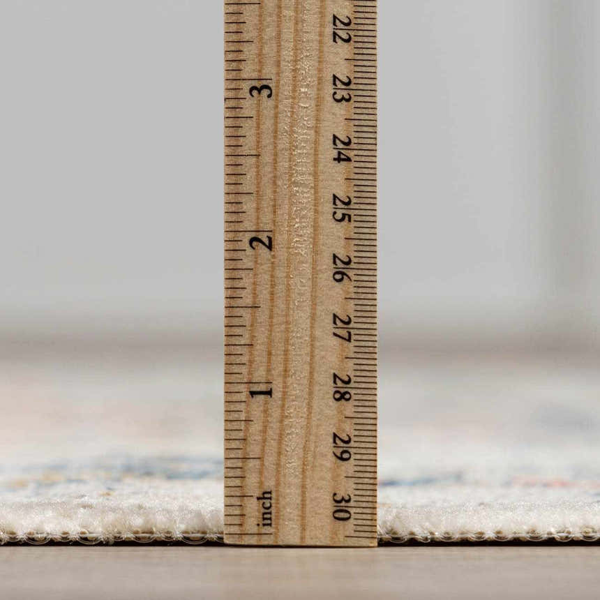 Close-up of the Dorval Traditional Rug pile height, measured with a ruler. Cream, blue, and peach colors visible. Pile