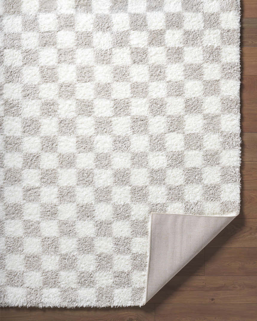Close-up of the Ardice Area Rug, a shag rug with an ivory and peach checkerboard pattern on hardwood floors. Fold
