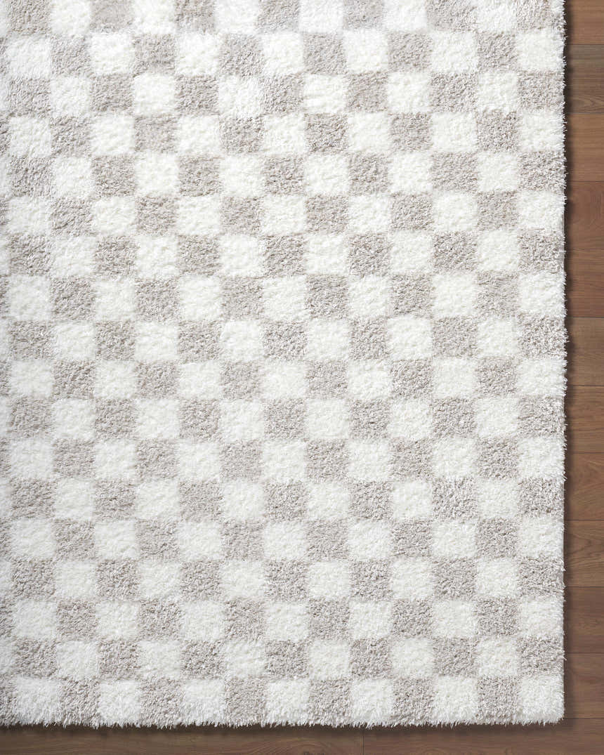 Close-up of the Ardice Area Rug, a shag rug with an ivory and peach checkerboard pattern on wood flooring. Corner