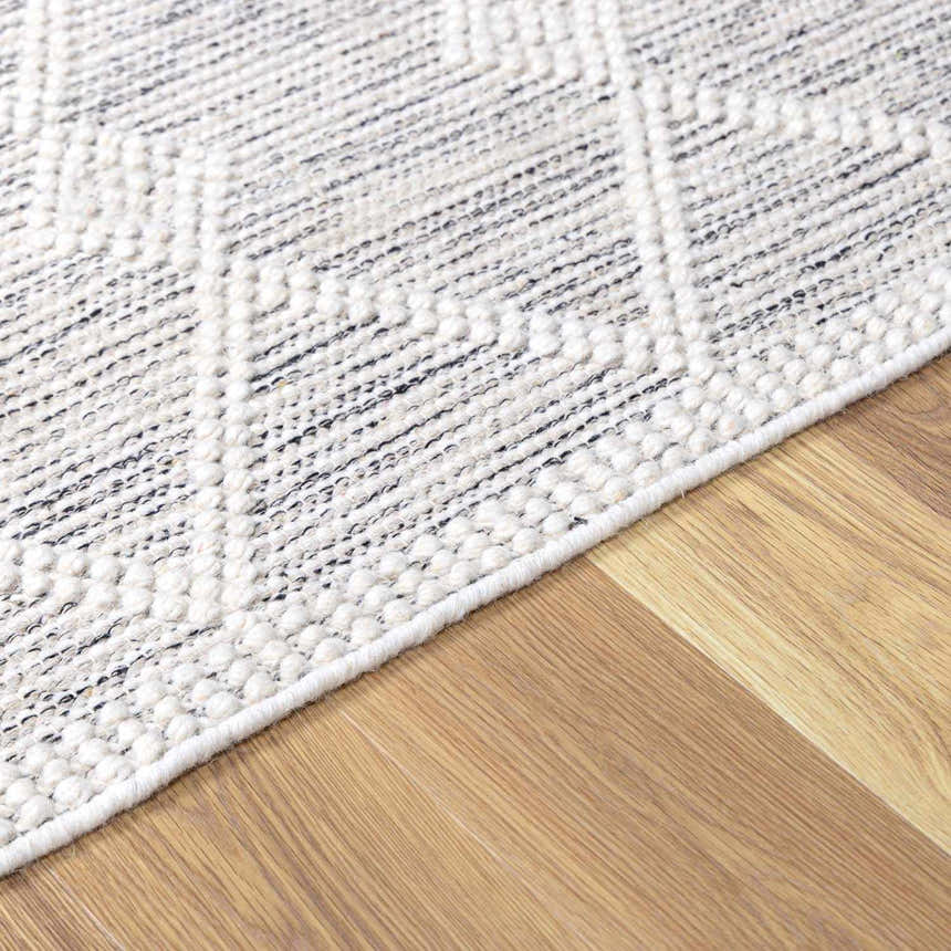 Close up of the New Whittington Area Rug. Hand woven wool rug in off white and gray with a geometric pattern. Corner