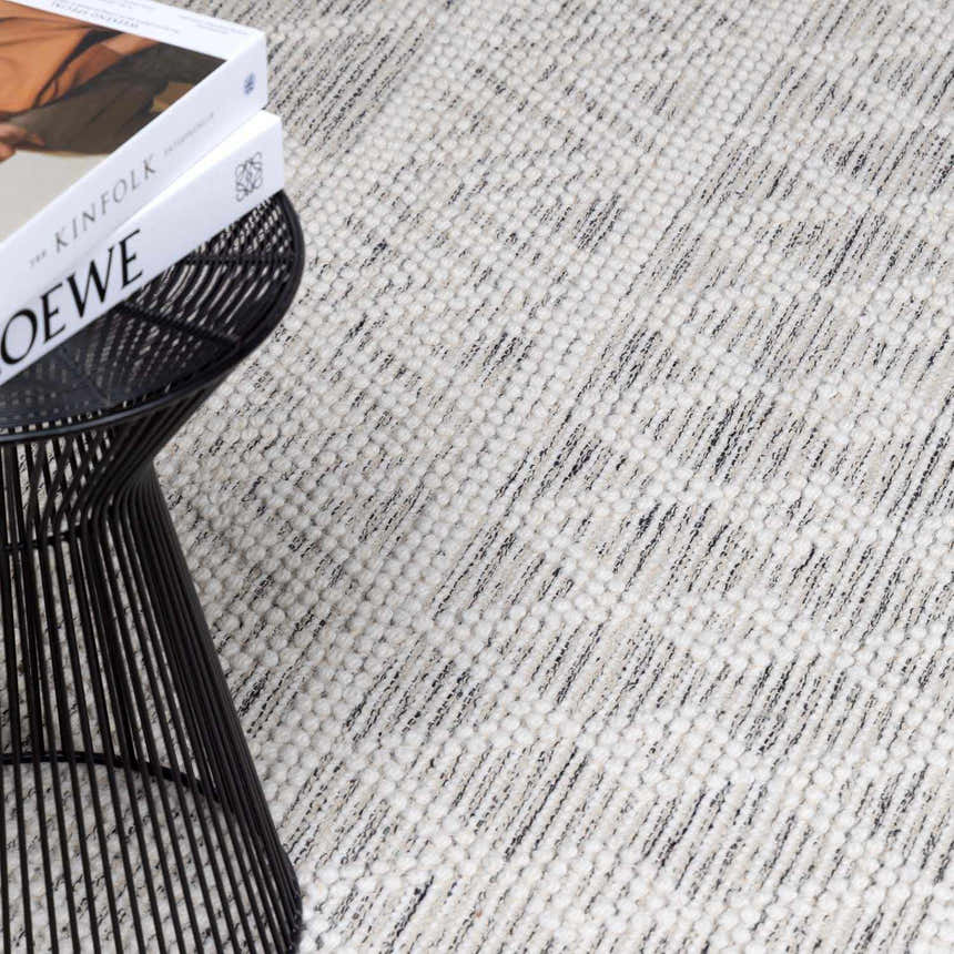 Close-up of the hand woven New Whittington Area Rug. The rug is off white and gray with a subtle geometric design. Styleshot