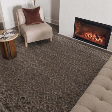 Living room scene with a gray Ironia Handmade Faux Silk Rug, fireplace, chair, and tufted ottoman. Roomscene-Rectangle