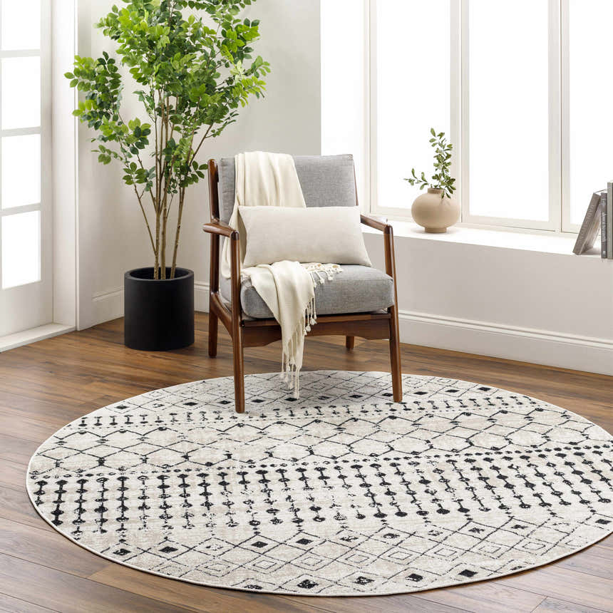 Living room scene with a round Joppatowne Washable Area Rug in black and cream under a gray chair with a throw. Roomscene-Round